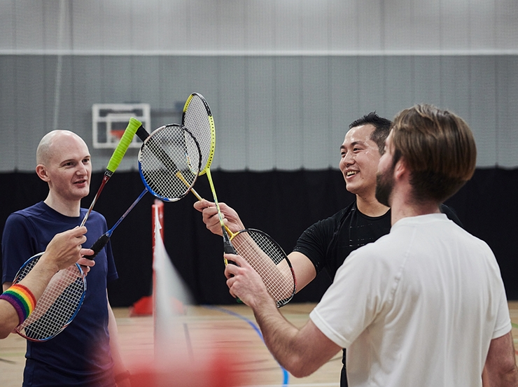 Three men hold badminton rackets together in a huddle